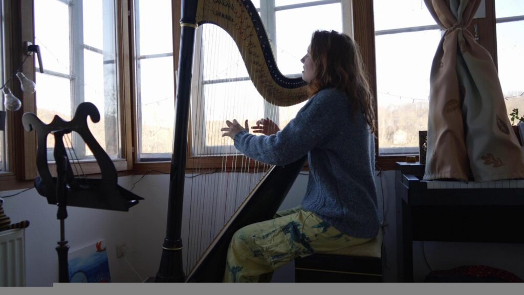 A white person with red hair plays harp and sings